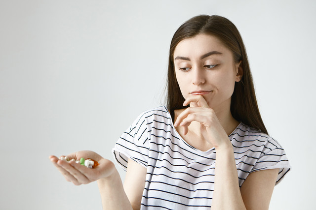 isolated-indecisive-doubtful-young-lady-with-loose-dark-hair-rubbing-chin-thoughtfully-looking-colorful-pills-her-palm-going-tak