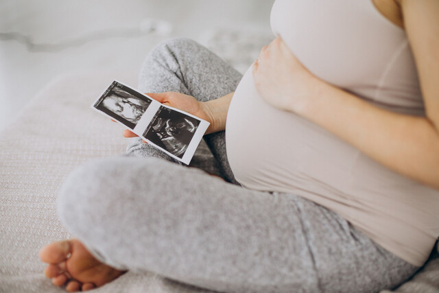 pregnant-woman-with-ultrasound-photo-sitting-bed.jpg